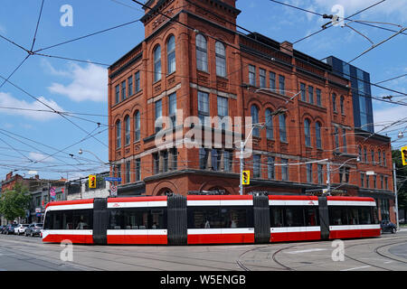 TORONTO - Juli 2019: Eine moderne artikulieren Straßenbahn biegt um eine Ecke, vor einem alten Hotel im Viktorianischen Stil in der Queen Street. Stockfoto