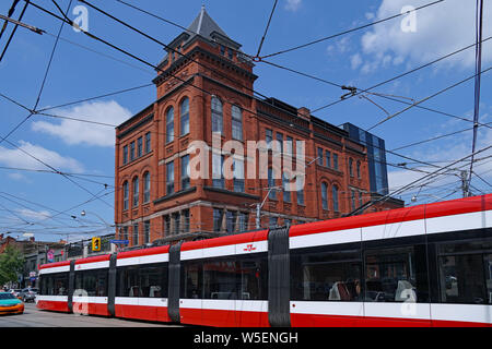 TORONTO - Juli 2019: Eine moderne artikulieren Straßenbahn vorbei an ein altes viktorianisches Hotel in der Queen Street. Stockfoto