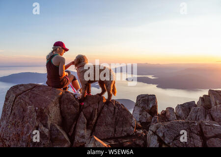 Abenteuerliche Mädchen ist Wandern mit Hund auf St. Mark's Mountain während eines sonnigen Sommer Sonnenuntergang. In West Vancouver, British Columbia, Kanada. Stockfoto