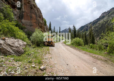 Traktor auf einer gebirgsstraße unter den Bergen und Nadelwälder. Kirgisistan. Naryn Region Stockfoto