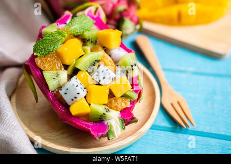 Mix tropischen Früchte, Salat serviert in einem halben Drachen Frucht auf hölzernen Tisch Stockfoto