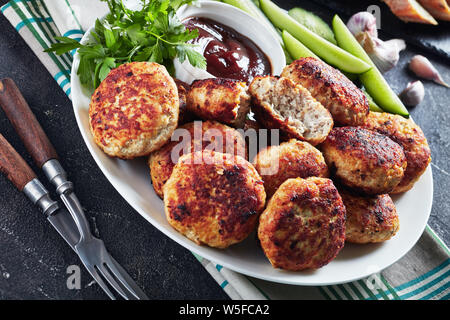 Polnische Fleischpflanzerl mit Gurkenscheiben und Barbeque Sauce auf einem weißen Teller auf einen konkreten Tisch serviert, horizontale Ansicht von oben, close-up Stockfoto