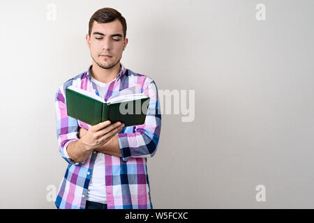 Junge Kaukasier Männlich Student in Plaid Shirt lesen Buch auf grauem Hintergrund mit Kopie Raum Stockfoto