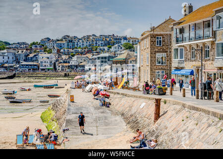 Sonnenanbeter, Familien, Shopper, Touristen und eine feine Cornish Pause am Meer auf der Hafenseite von St Ives auf einer belebten schöner Frühling sonnigen Tag. Stockfoto