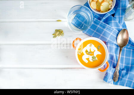 Selbstgemachte Kürbissuppe in Keramik Schüssel mit Samen, saure Sahne und Brot Croutons auf weißen Holzmöbeln im Landhausstil Hintergrund Stockfoto