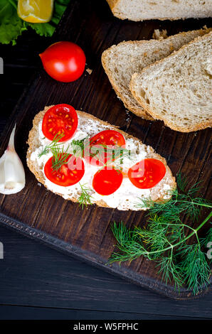 Roggen Brot Sandwiches mit weichen Mozzarella oder Feta Käse und Tomaten auf einem dunklen rustikalen Tisch aus alten Boards Stockfoto