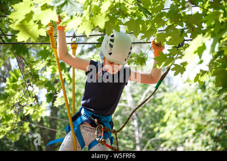 8 Jahre altes Mädchen in Forest Adventure Park. Kind klettern im Hochseilgarten Trail. Spielplatz im Freien mit Seil weg. Stockfoto