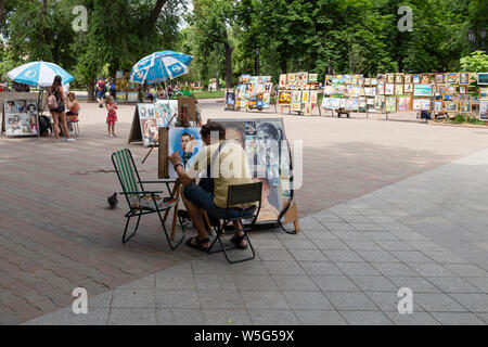 Ukraine, Odessa, Preobrazhenska Straße, 12. Juni 2019. Ein street artist arbeitet an einem Cartoon Stil Portrait Malerei auf dem Platz vor dem Stockfoto