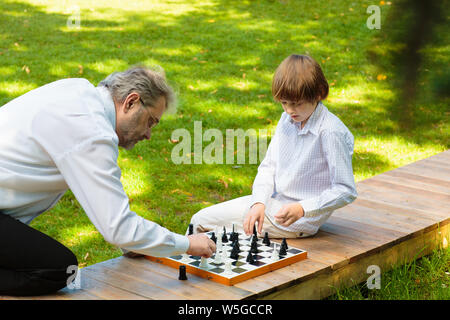 Großvater, Vater und Kinder spielen Schach im Sommer Garten. Opa, Vater und kleiner Junge Brettspiele spielen. Familie, Generationen und Liebe. Stockfoto