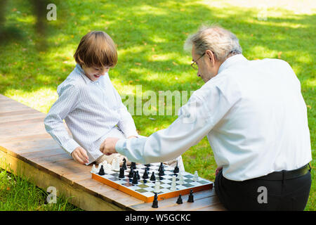 Großvater, Vater und Kinder spielen Schach im Sommer Garten. Opa, Vater und kleiner Junge Brettspiele spielen. Familie, Generationen und Liebe. Stockfoto