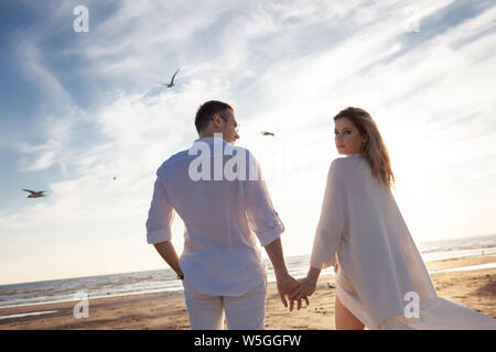 Liebe, Romantik am Strand. Junge schöne Paar, Frau, Mann, in weißen Lose flying Kleidung, gehen, Hände halten, entlang der Küste. Stockfoto