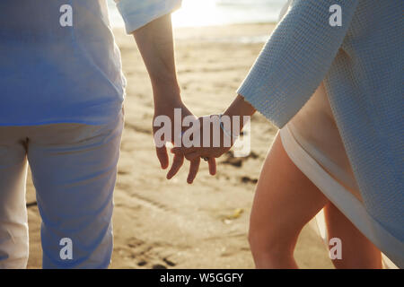 Liebe, Romantik am Strand. Junge schöne Paar, Frau, Mann, in weißen Lose flying Kleidung, gehen, Hände halten, entlang der Küste. Stockfoto