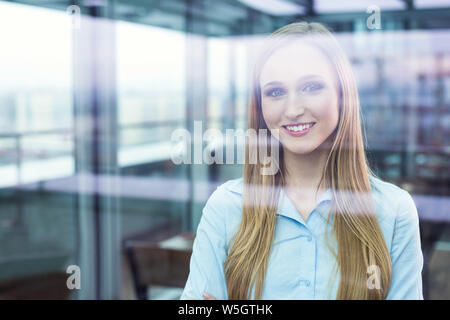 Junge optimistische Geschäftsfrau Blick durch ein Bürofenster Stockfoto