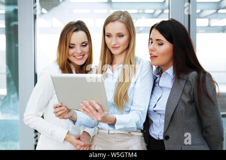Gruppe von drei Geschäftsfrauen an einem digitalen Tablet von einer von ihnen gehaltenen suchen Stockfoto