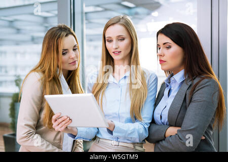 Gruppe von drei jungen Unternehmerinnen an einem digitalen Tablet zu schauen und zu reden Stockfoto