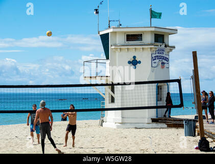 Laguna Beach, CA/USA: 10. März 2019: Main Beach. Männer Beachvolleyball spielen, während Touristen warten, Fotos vor Wahrzeichen lifeguard Tower zu nehmen. Stockfoto