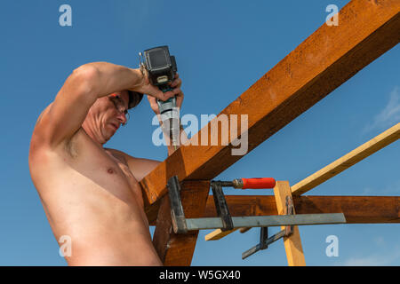 Ein Tischler auf dem Dach Bohrer Loch in Holz mit Akkuschrauber Stockfoto