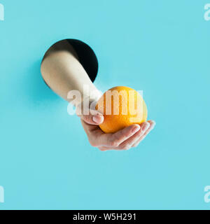 Weibliche Hand, die eine reife orange blau Papier Loch. Stockfoto