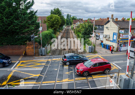 Autos fahren durch ein Bahnübergang außerhalb Datchet Bahnhof. Barrieren sind. Bahngleise verschwinden in der Ferne. Stockfoto