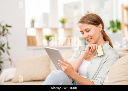 Hübsches Mädchen mit Touchpad und Plastikkarte suchen durch Waren im Online Shop Stockfoto