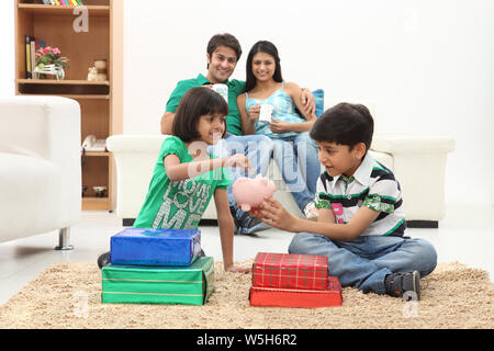 Mädchen, das mit ihrem Bruder eine Münze in ein Sparschwein legt Stockfoto