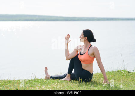 Ruhige junge Frau im Sport Kleidung sitzen auf Gras am See Stockfoto