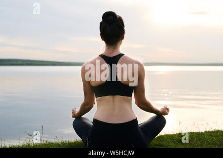 Ansicht der Rückseite des jungen Frau in Schwarz sportswear Sitzen mit gekreuzten Beinen Stockfoto