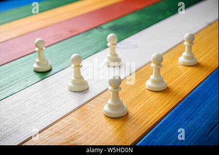 White pawn Schachfiguren auf einem farbenfrohen Schreibtisch von holzbohlen platziert. Stockfoto