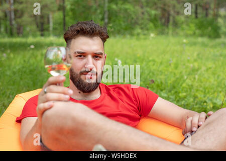 Freizeitaktivitäten Konzept, Camping, Sommerferien. Junge Bartgeier kaukasischen Mann mit Gläsern Wein zur Festlegung von Orange Sofa. Entspannen und genießen das Leben auf der Luft b Stockfoto