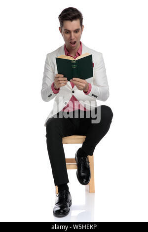 Excitd eleganten Mann sitzen und ein gutes Buch lesen und er schaut überrascht und erstaunt auf weißem Hintergrund Stockfoto