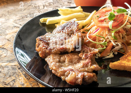 Gebratenes Schweinefleisch steak in schwarz Platte auf dem Holztisch. Stockfoto