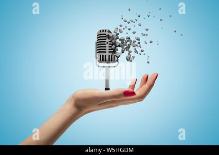 Weibliche Hand, die Vintage Mikrofon zerbricht in Stücke auf blauem Hintergrund Stockfoto
