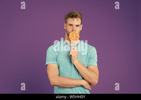 Mann mit Borsten mag Lollipop. Cheat meal Konzept. Zucker schädlich für die Gesundheit. Kerl halten Lollipop candy violett unterlegt. Mann schöner macho Essen großen bunten süßen Lutscher. Geschmack der Kindheit. Stockfoto