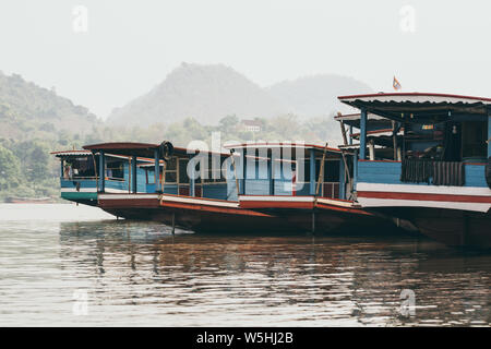 Die traditionellen laotischen Holz langsam Boote am Mekong River in der Nähe von Luang Prabang, Laos bei Sonnenuntergang. Die Berge im Hintergrund Stockfoto