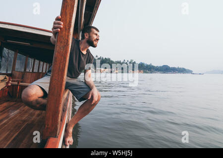 Junge kaukasier bärtiger Mann mit einem Sonnenuntergang Bootsfahrt auf dem Mekong in Luang Prabang, Laos Stockfoto