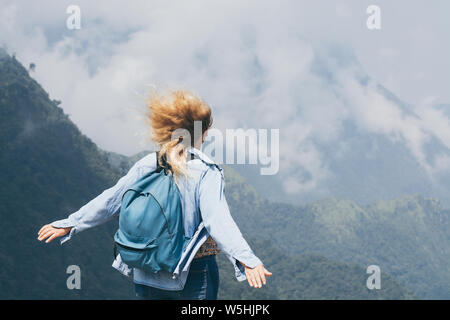 Kaukasische blonde junge Frau trinkt Kaffee in der Straßenbahn Tonne Pass mit Blick auf die Berge um Sapa in Vietnam. Hände hoch, Wind im Haar. Stockfoto