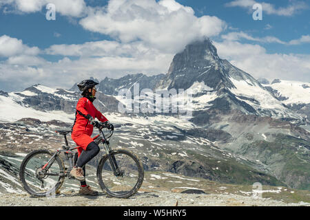 Active Senior, Frau, reiten Ihr elektrische Mountainbike unterhalb des berühmten Matterhorns in Zermatt, Wallis, Schweiz Stockfoto