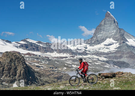 Active Senior, Frau, reiten Ihr elektrische Mountainbike unterhalb des berühmten Matterhorns in Zermatt, Wallis, Schweiz Stockfoto