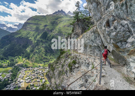 Aktive Senior-Frau, die ihr Elektro-Mountainbike auf einem schmalen Mountainbike-Trail hoch über Zermatt, dem berühmten Touristenziel im südwesten, schiebt Stockfoto