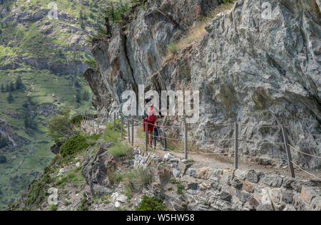 Aktive Senior-Frau, die ihr Elektro-Mountainbike auf einem schmalen Mountainbike-Trail hoch über Zermatt, dem berühmten Touristenziel im südwesten, schiebt Stockfoto