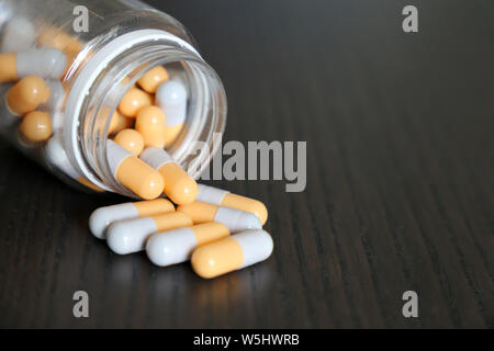 Kapseln verschüttete aus der Flasche, weiß-gelbe Pillen auf Vintage dunklen Holztisch. Konzept der Apotheke, Antibiotika, Vitamine Stockfoto