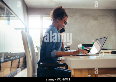 Seitenansicht der Schoß der Frau am Telefon sprechen und lächelnd während der Arbeit am Laptop. Geschäftsfrau in Ihrem Büro arbeiten. Stockfoto