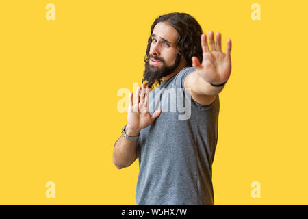 Stoppen. Portrait von verwirrten jungen Mann mit langen lockigen Haar grau tshirt stehend mit stop Handzeichen Geste bärtigen erschrocken oder und Kamera. Stockfoto
