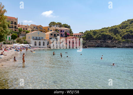 Anzeigen von Assos Dorf auf der griechischen Insel Kefalonia mit Booten und bunte Häuser mit Sonnenanbeter am Strand und Schwimmen Stockfoto