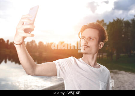 Porträt der jungen schönen stilvollen lächelnden Kerl macht selfie gegen den Strand. Schöne Natur Stockfoto