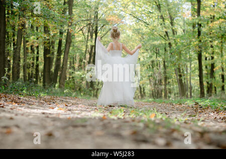 Ein kleines Mädchen im Kleid tanzen im Weg unter den herbstlichen Bäume im Wald im Goldenen Stunde Atmosphäre Stockfoto