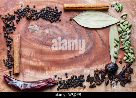 Typische Zutaten für einen Garam Masala schwarze Pfefferkörner, Muskatblüte, Zimt, Nelken, getrocknete rote Chili und grünen Kardamom in einer Holz- Hintergrund Stockfoto