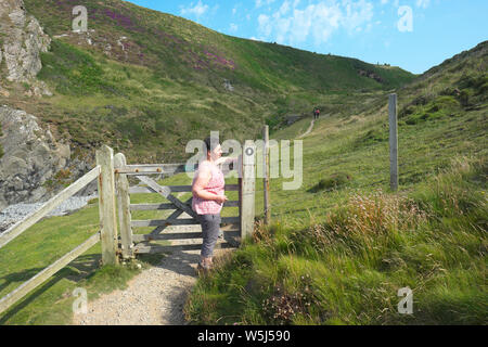 Eine weibliche Walker auf der Pembrokeshire Coast Path öffnet ein Tor auf dem Fußweg in der Nähe von Solva im Sommer Juli 2019 Stockfoto