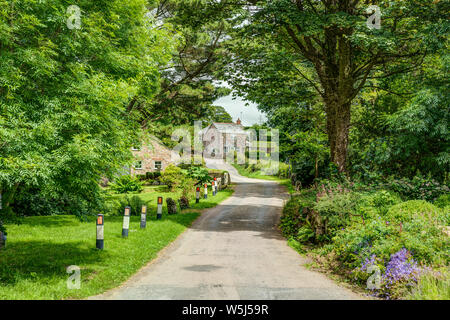 Eine idyllische Landschaft einer typisch englischen Dorf auf dem Land im Sommer. Eine Wicklung mit Bäumen gesäumten Weg über eine kleine Brücke mit einem Cottage in der Ferne Stockfoto