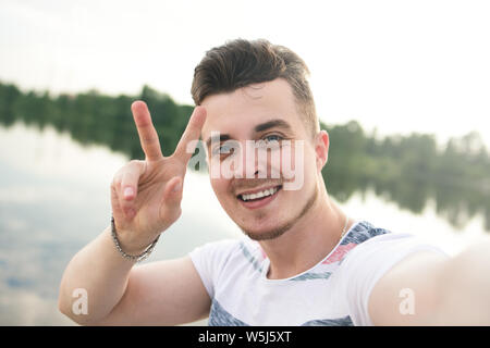 Porträt der jungen schönen stilvollen lächelnden Kerl macht selfie gegen den See. schöne Natur Stockfoto